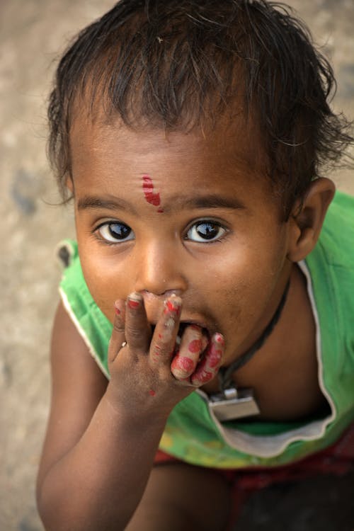 Little ethnic girl eating from palm on ground