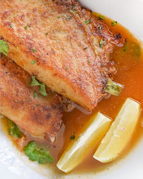 Close-up of fried fish paired with lemon wedges and garnished with herbs.