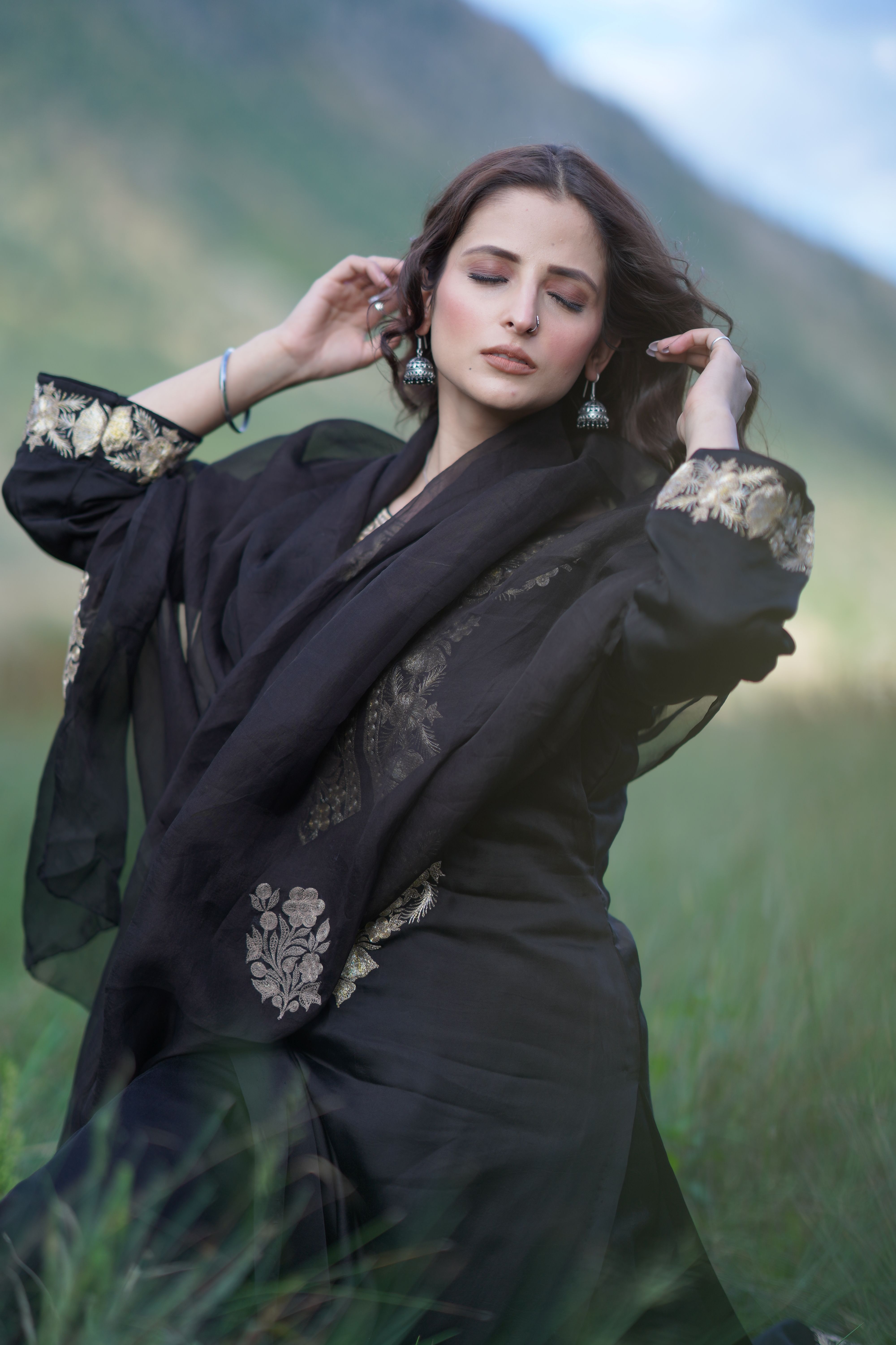 Portrait of a woman in black traditional dress with closed eyes, outdoors in nature.