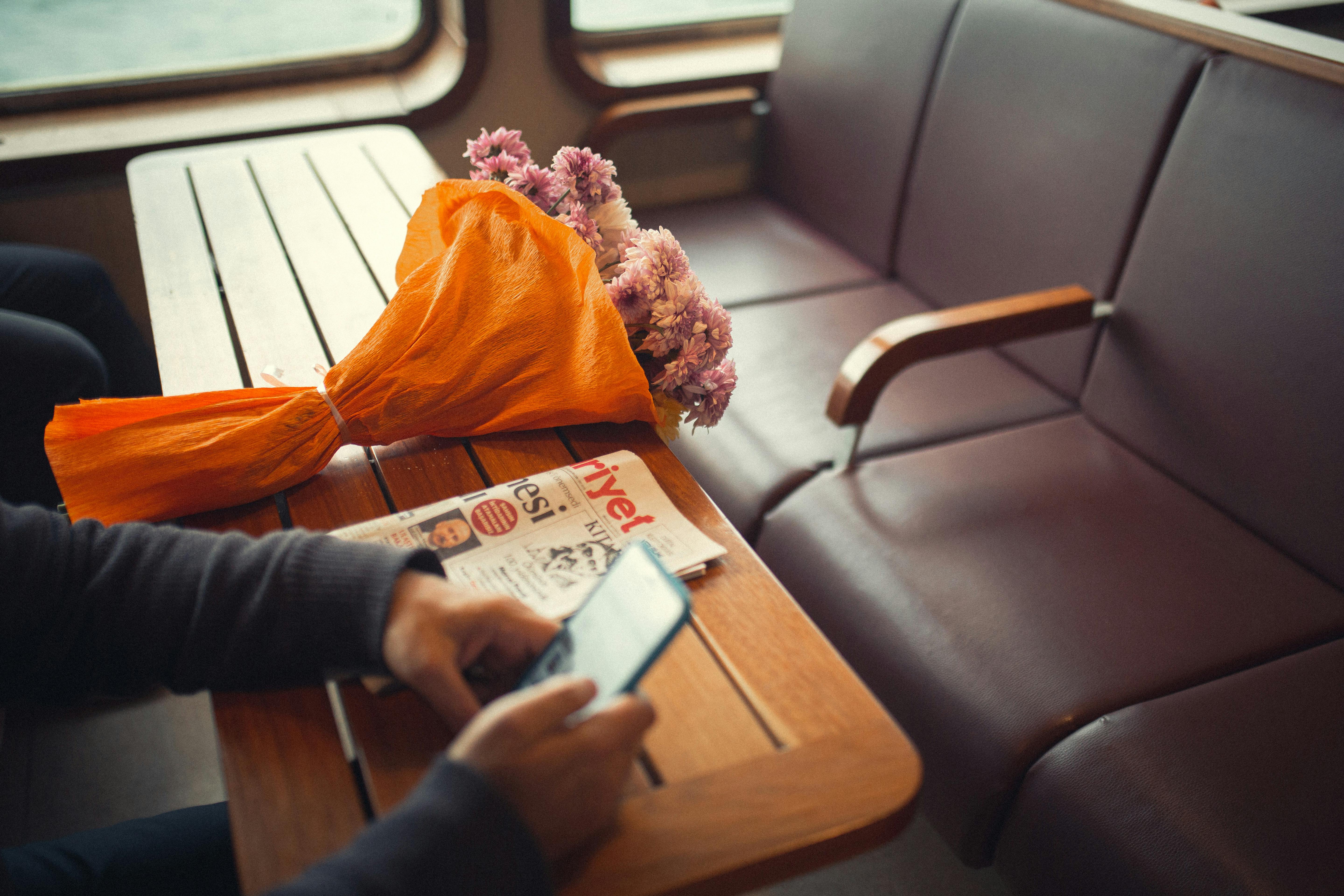A bouquet of flowers on a ferry table beside a person using a smartphone, traveling in Istanbul.
