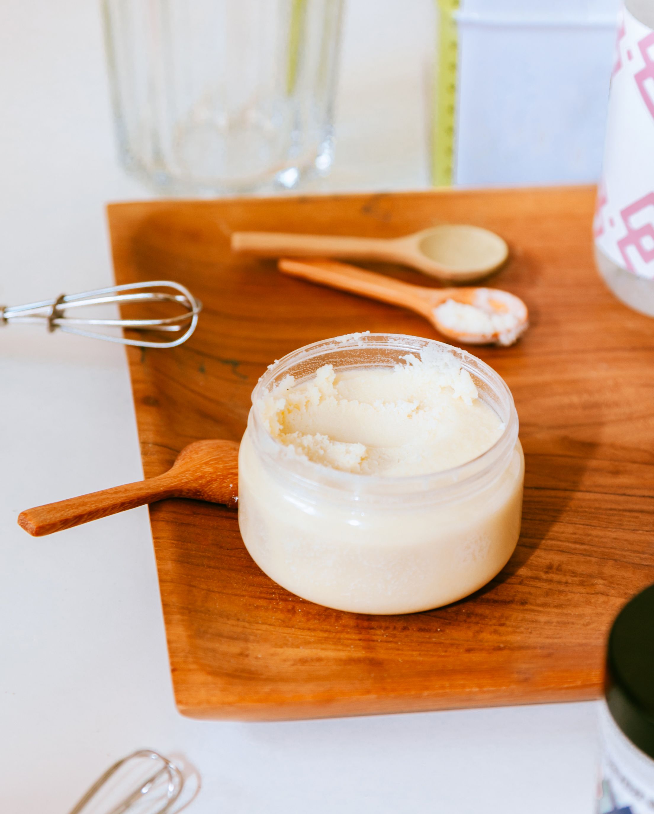 A close-up of creamy butter in a container on a wooden cutting board with kitchen utensils.