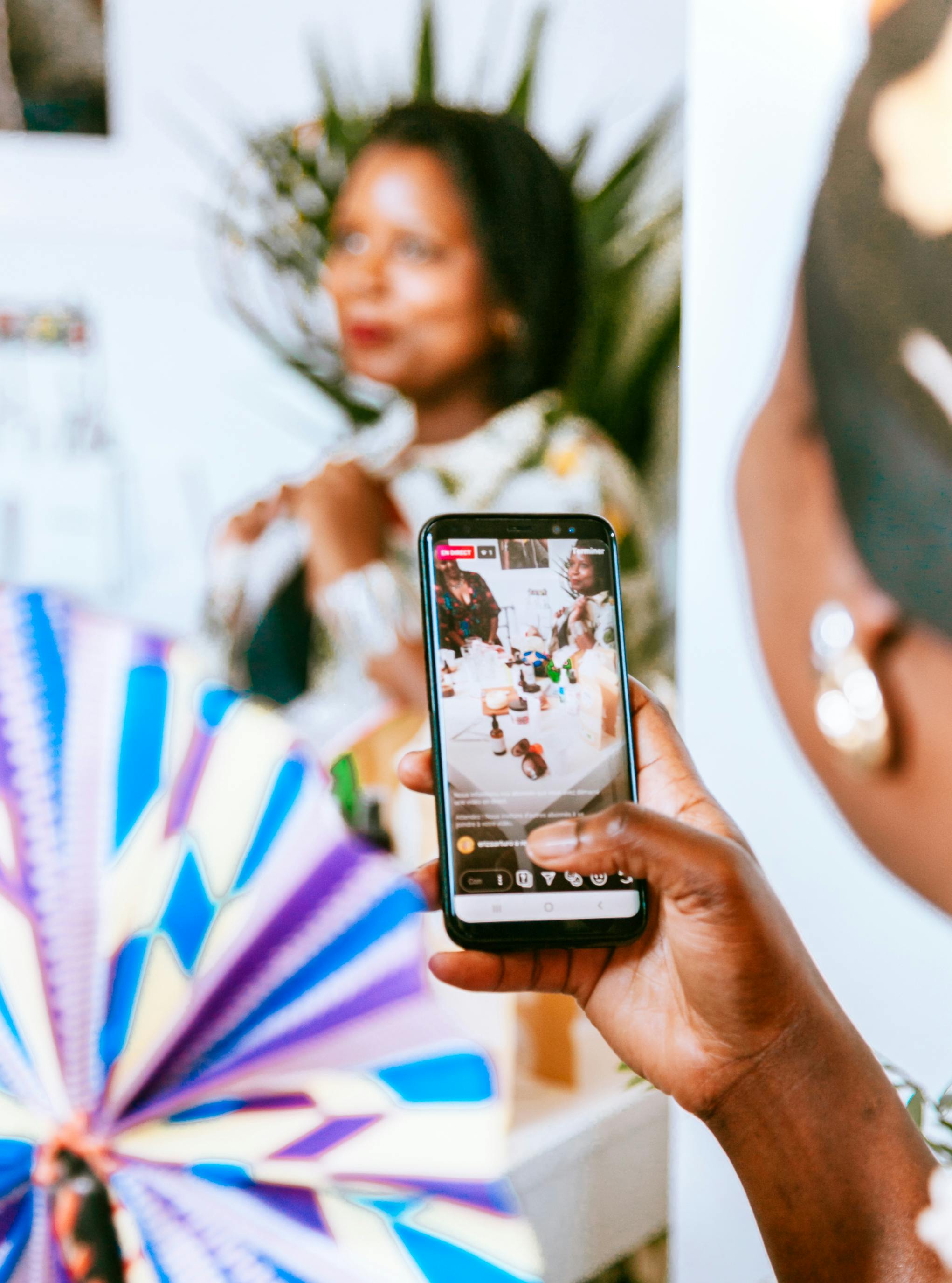 A person holds a smartphone capturing a live event with vibrant colors in the background.