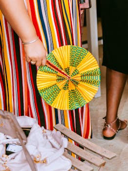 Vibrant African-inspired fashion showing a woman in a colorful striped dress and hand fan. Perfect for cultural themes.