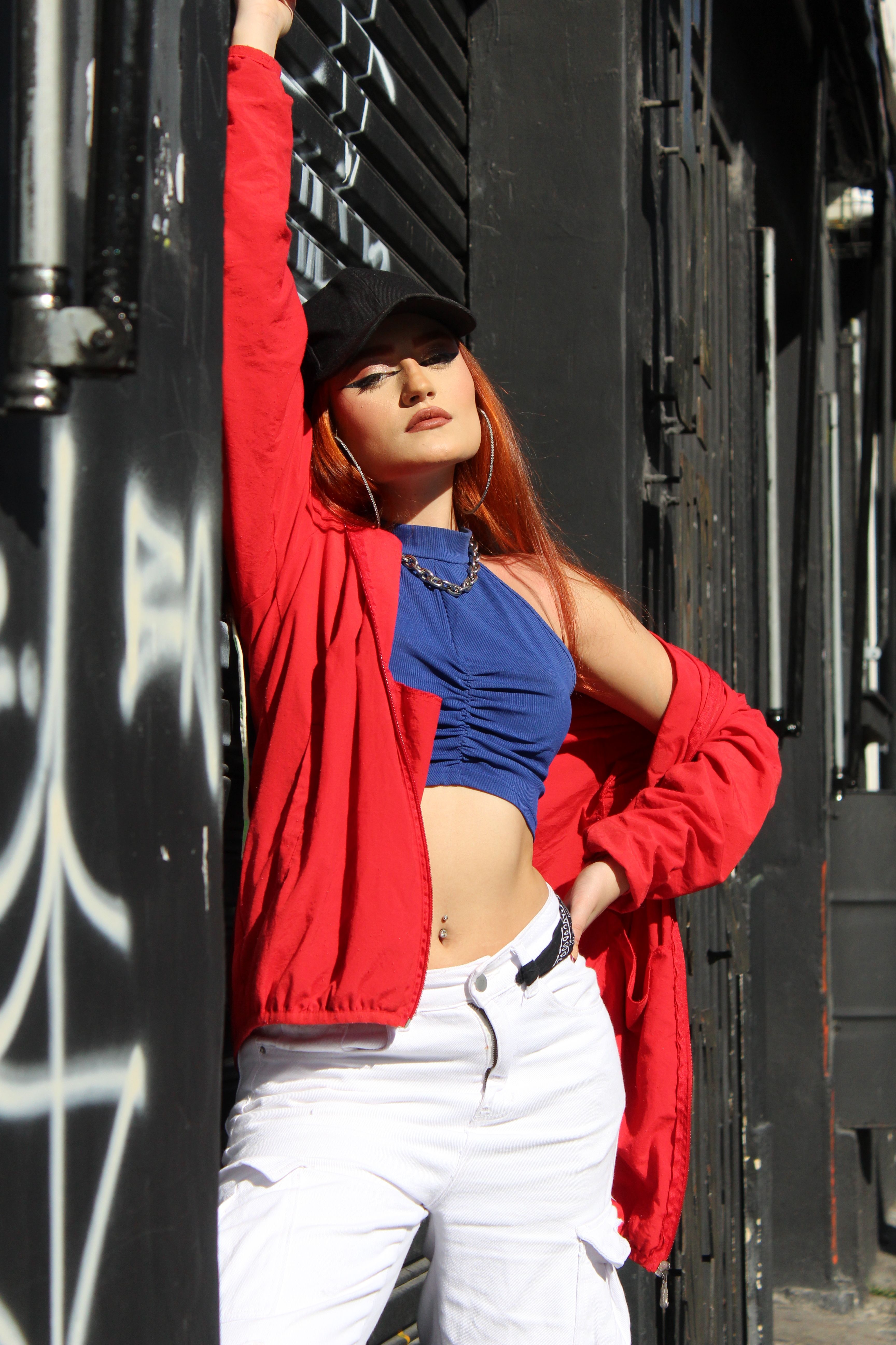 Fashionable woman in red jacket poses confidently against a graffiti-covered wall outdoors.