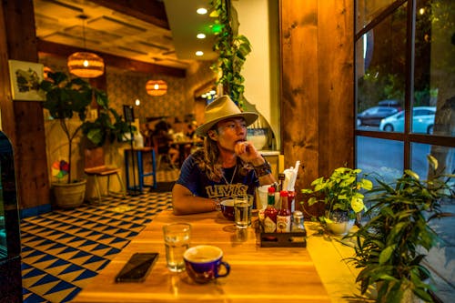 Man in a Hat Sitting at a Table in a Restaurant and Looking Out the Window 