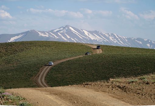 Capture of a dirt road leading through a stunning mountainous landscape with snow-capped peaks.