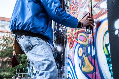 Free Street artist in Berlin adding vibrant graffiti to a wall with spray paint. Stock Photo