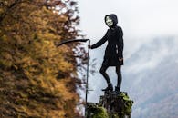 薄雾弥漫，一个戴着面具的人手持镰刀，站在秋叶中的树桩上