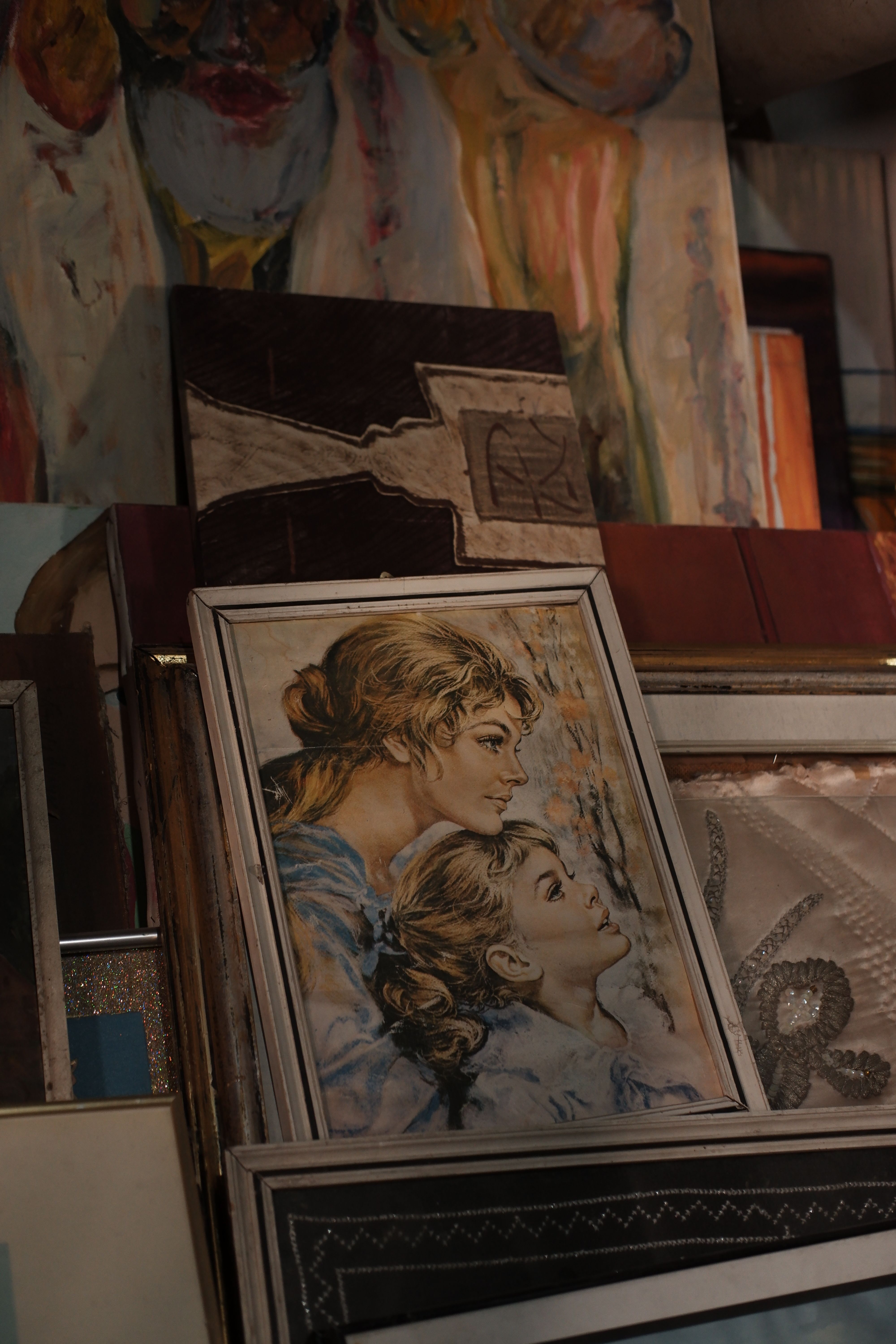 Fotomural Una obra de arte vintage que representa a una madre y a su hijo, enmarcada en madera, rodeada de varias pinturas.
