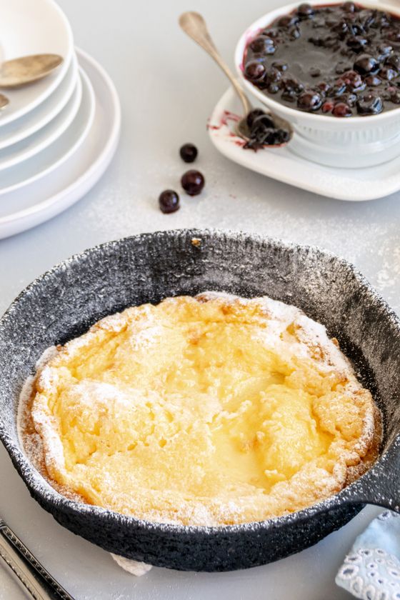 Golden Dutch baby pancake in a cast iron skillet dusted with powdered sugar, blueberry compote