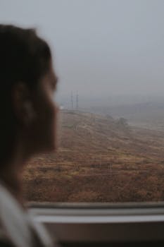 Woman gazing out a train window at a foggy landscape, evoking serenity and introspection.