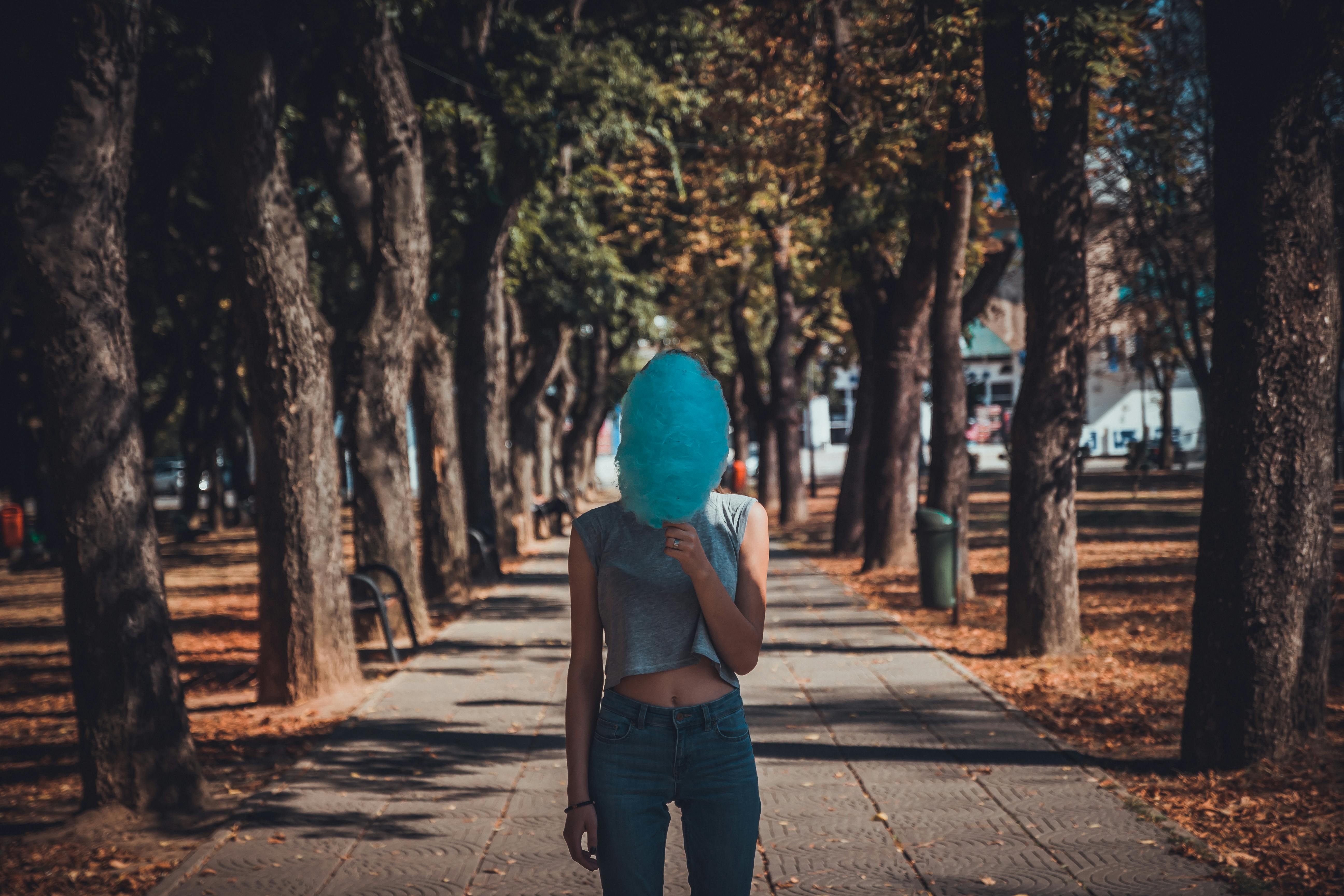 Woman hiding face with cotton candy on a shaded park pathway surrounded by trees in Oradea, Romania.