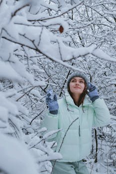 A woman in winter attire happily explores a snow-covered forest, embracing the cold season.