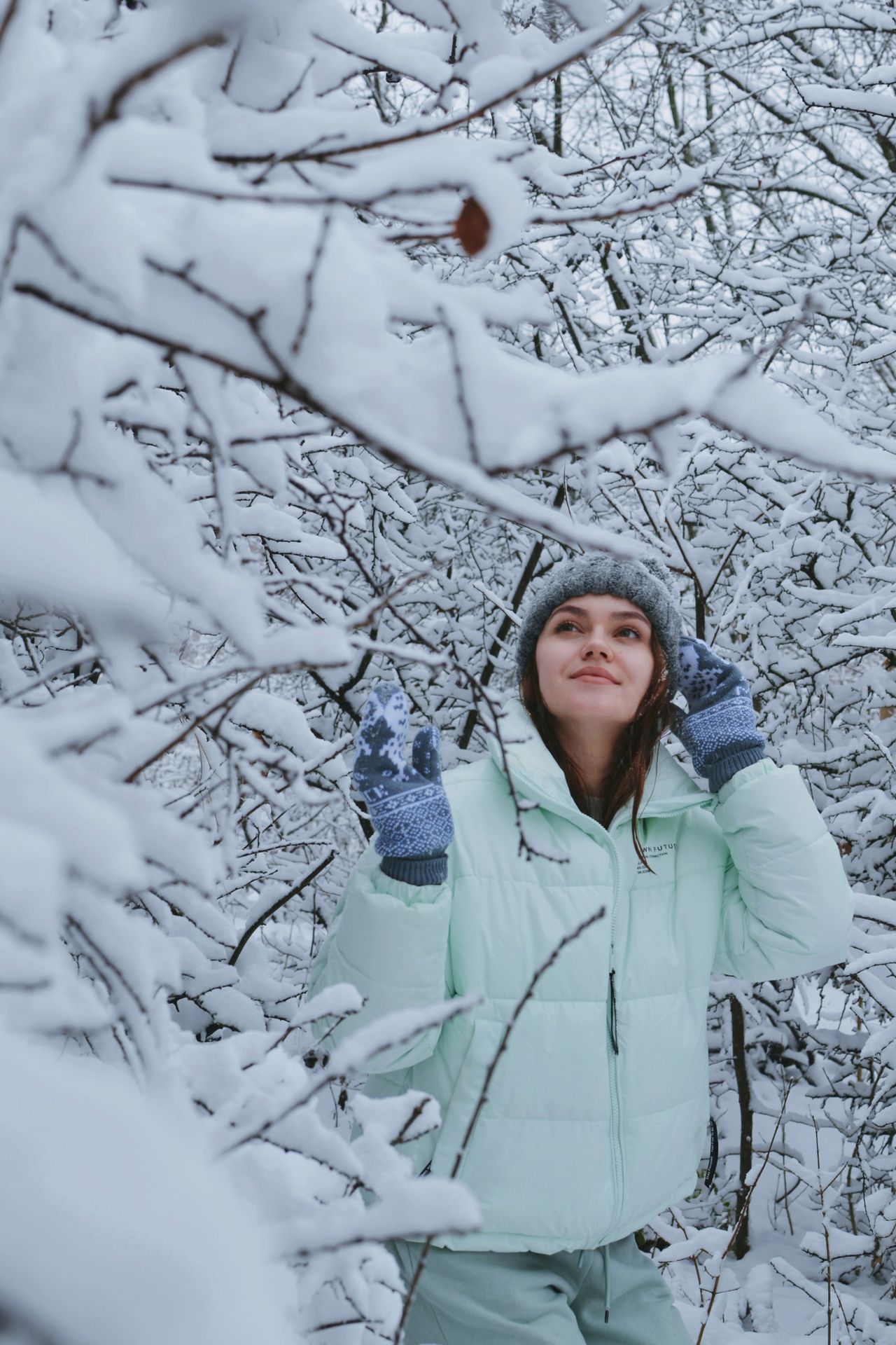 Woman in a white puffer jacket among snow-covered branches