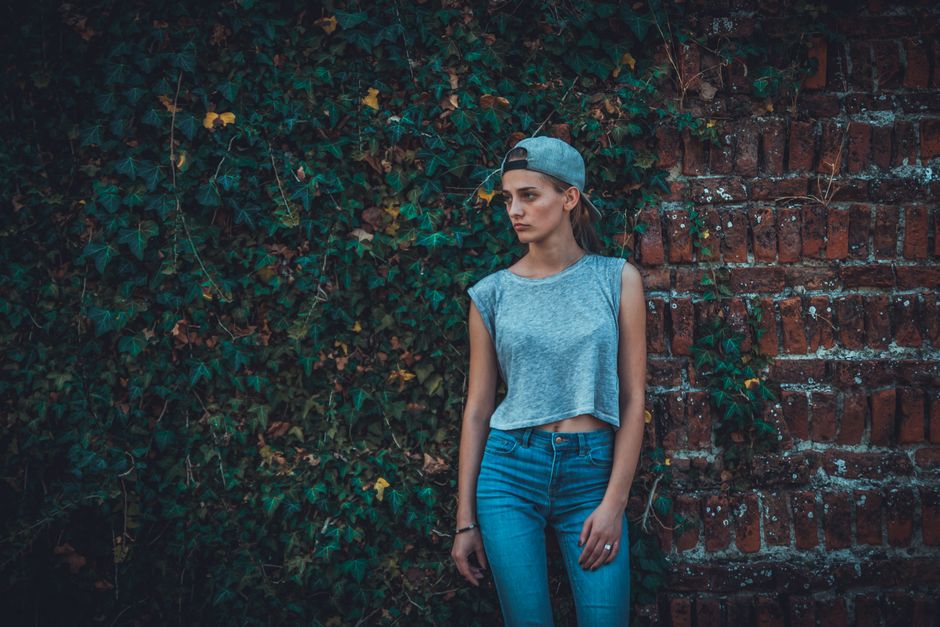 Stylish portrait of a young woman in casual wear against a brick wall with ivy.
