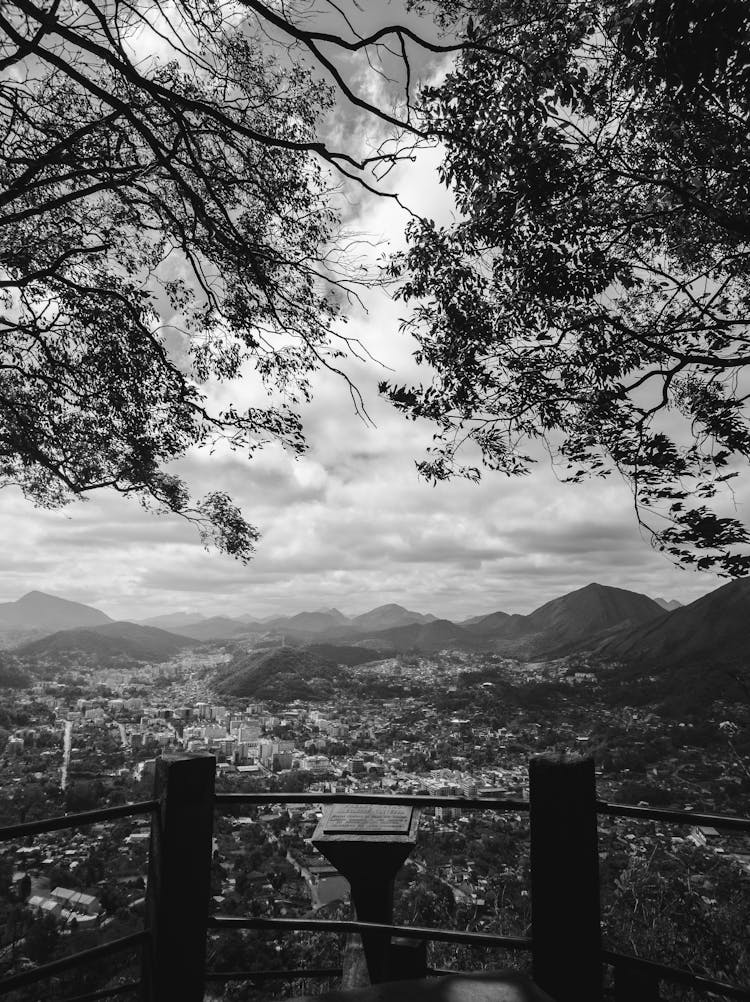 Mountain And Town Landscape Framed By Trees And A Railing