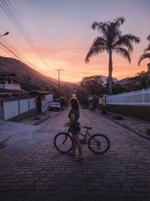 Photo of a Woman with a Bike Standing on the Road