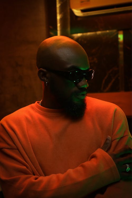 Free A fashionable man in an orange sweater and sunglasses in warm lighting. Stock Photo