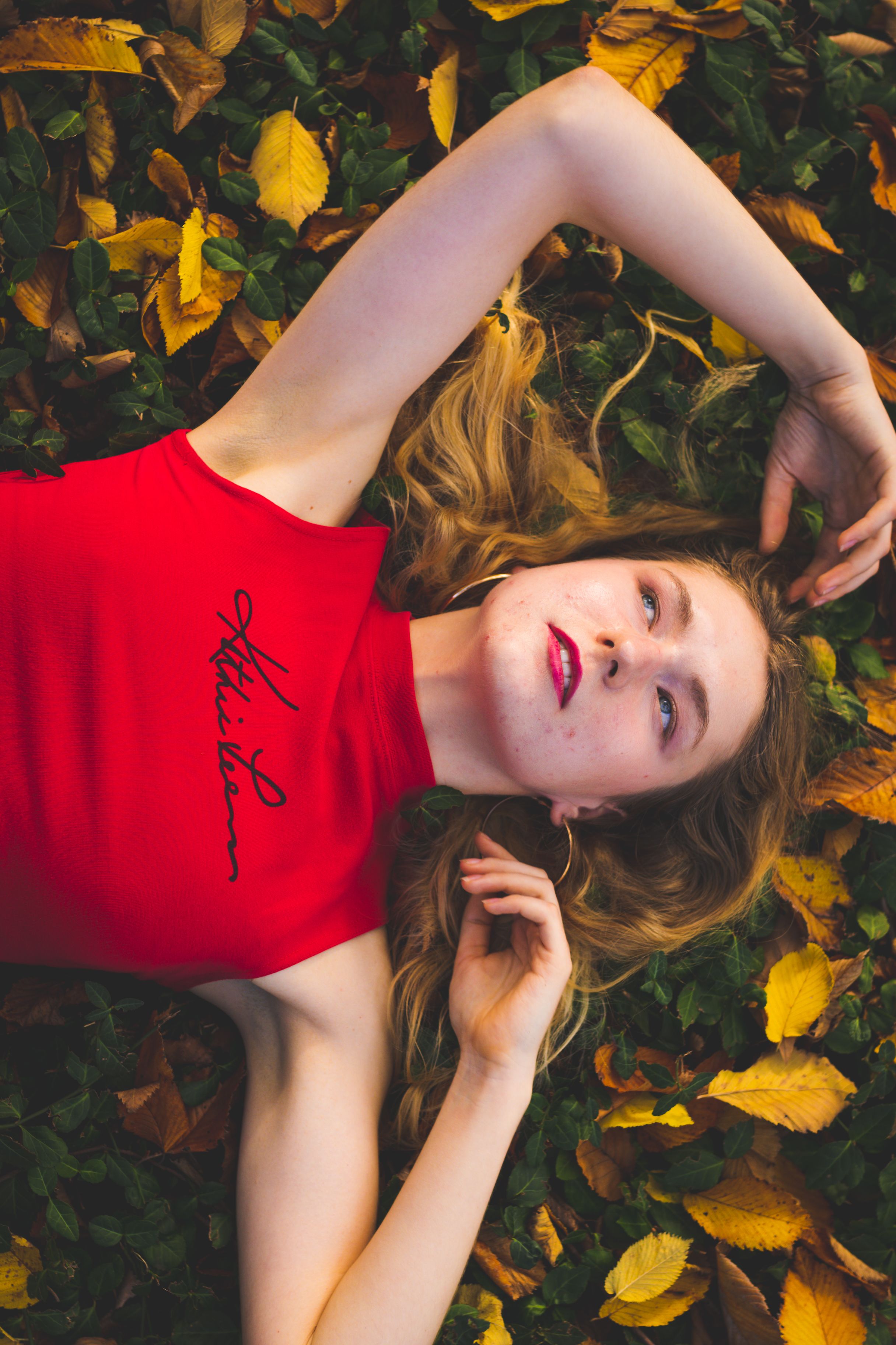 Stylish woman in red blouse posing on fall leaves, highlighting autumn fashion.