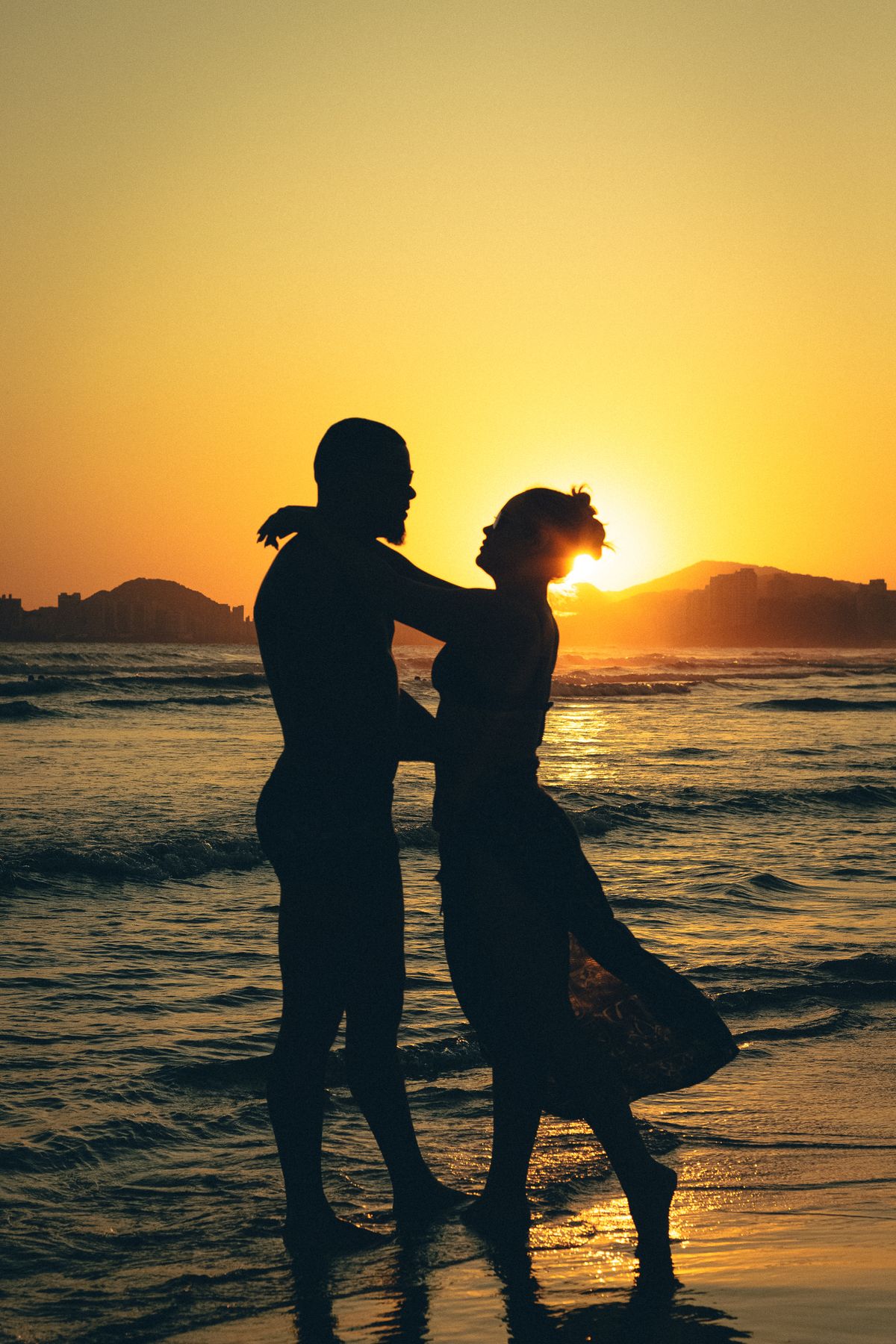 Silhouet van een koppel dat elkaar omhelst aan zee bij zonsondergang