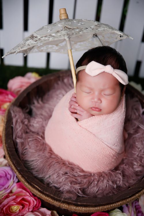 Free Cute sleeping newborn wrapped in pink with small lace umbrella, surrounded by flowers. Stock Photo