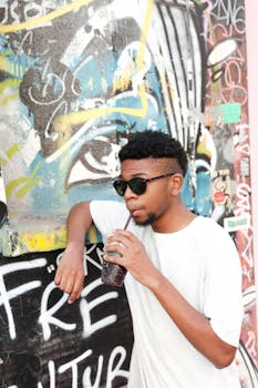Fashionable young adult sipping a beverage in front of colorful graffiti in an urban setting.