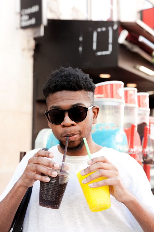 Free Young man with sunglasses sipping two colorful drinks outdoors in Kingston, Jamaica. Stock Photo