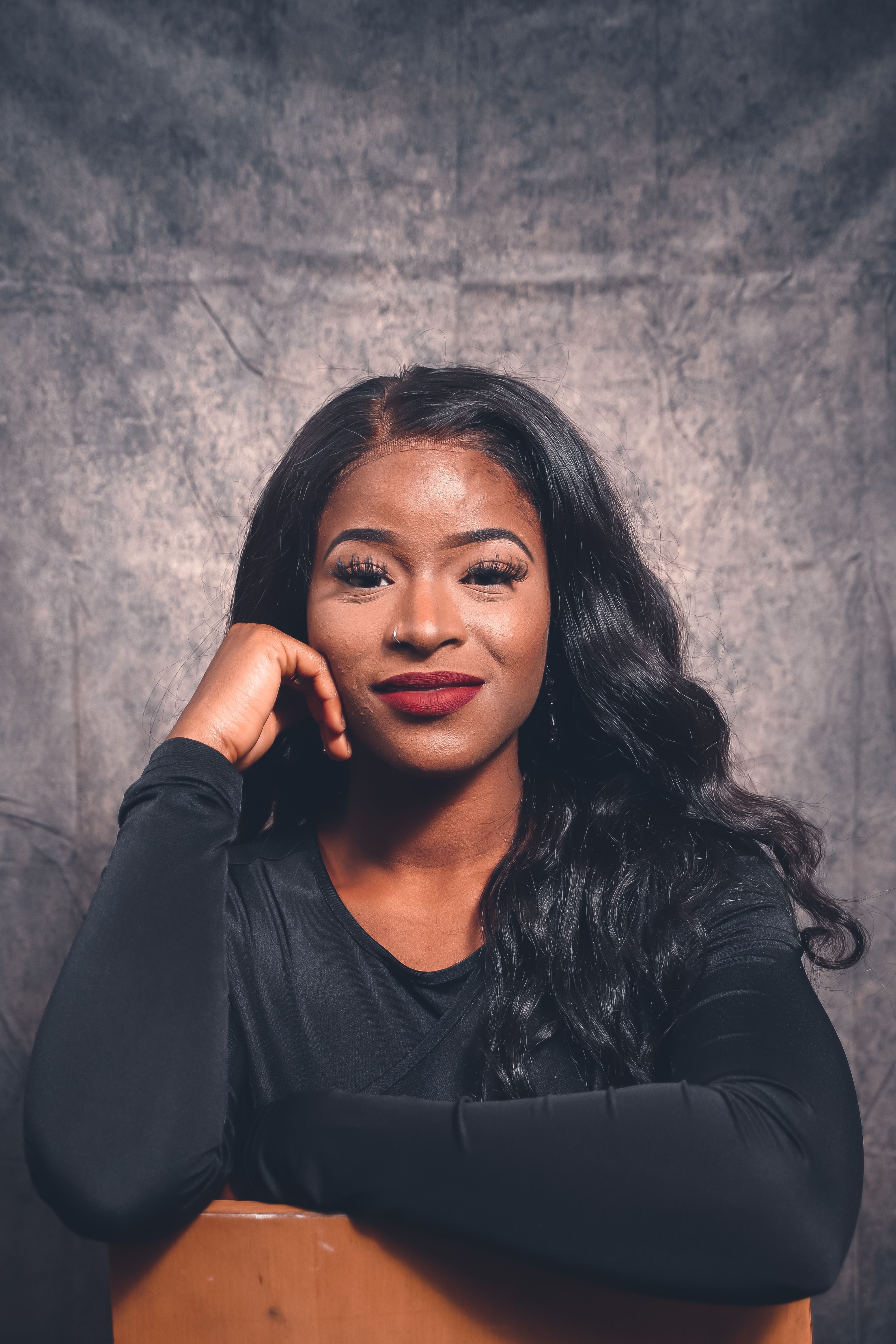 Striking portrait of a confident black woman in black attire, smiling against a textured backdrop.