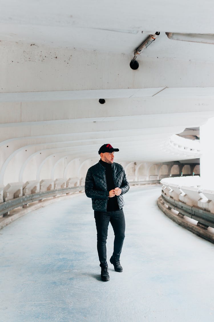 A Man In Black Jacket Walking While Wearing A Cap