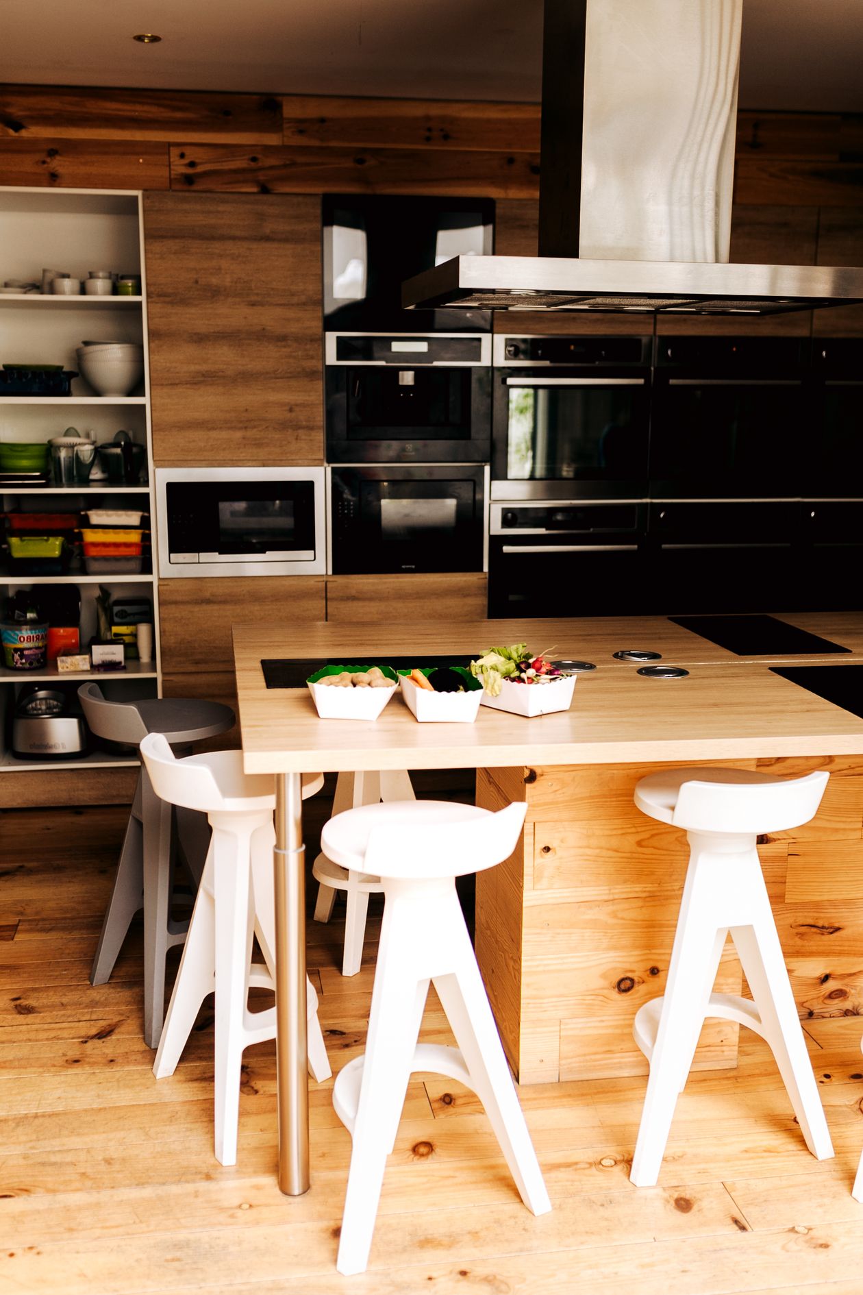 Modern wooden kitchen island with white bar stools and built-in oven tower