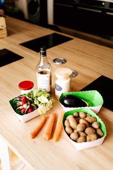 Assorted fresh vegetables and ingredients on a wooden kitchen table ready for food preparation.