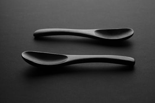 Artistic monochrome image of two wooden spoons on a dark surface, ideal for minimalist design. by Negative Design