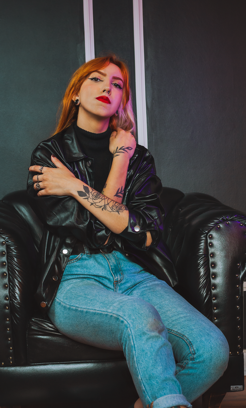 Free Confident woman in black jacket with tattoos seated on a leather chair indoors. Stock Photo