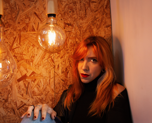 Free A woman with red lipstick poses under warm glowing light bulbs in a modern indoor setting. Stock Photo