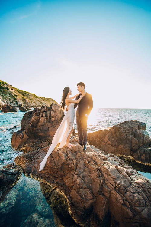 Man and Woman Standing on Brown Rock Under Blue Sky