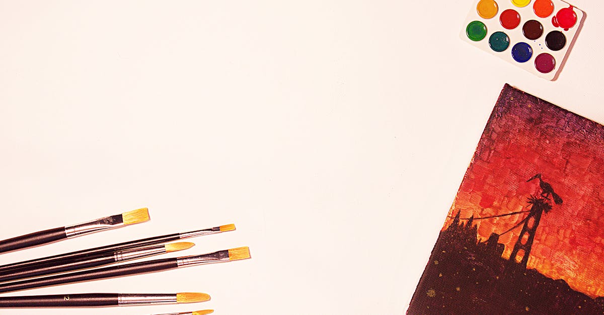 Flat lay of paintbrushes, watercolors, and a vivid canvas artwork with warm tones.