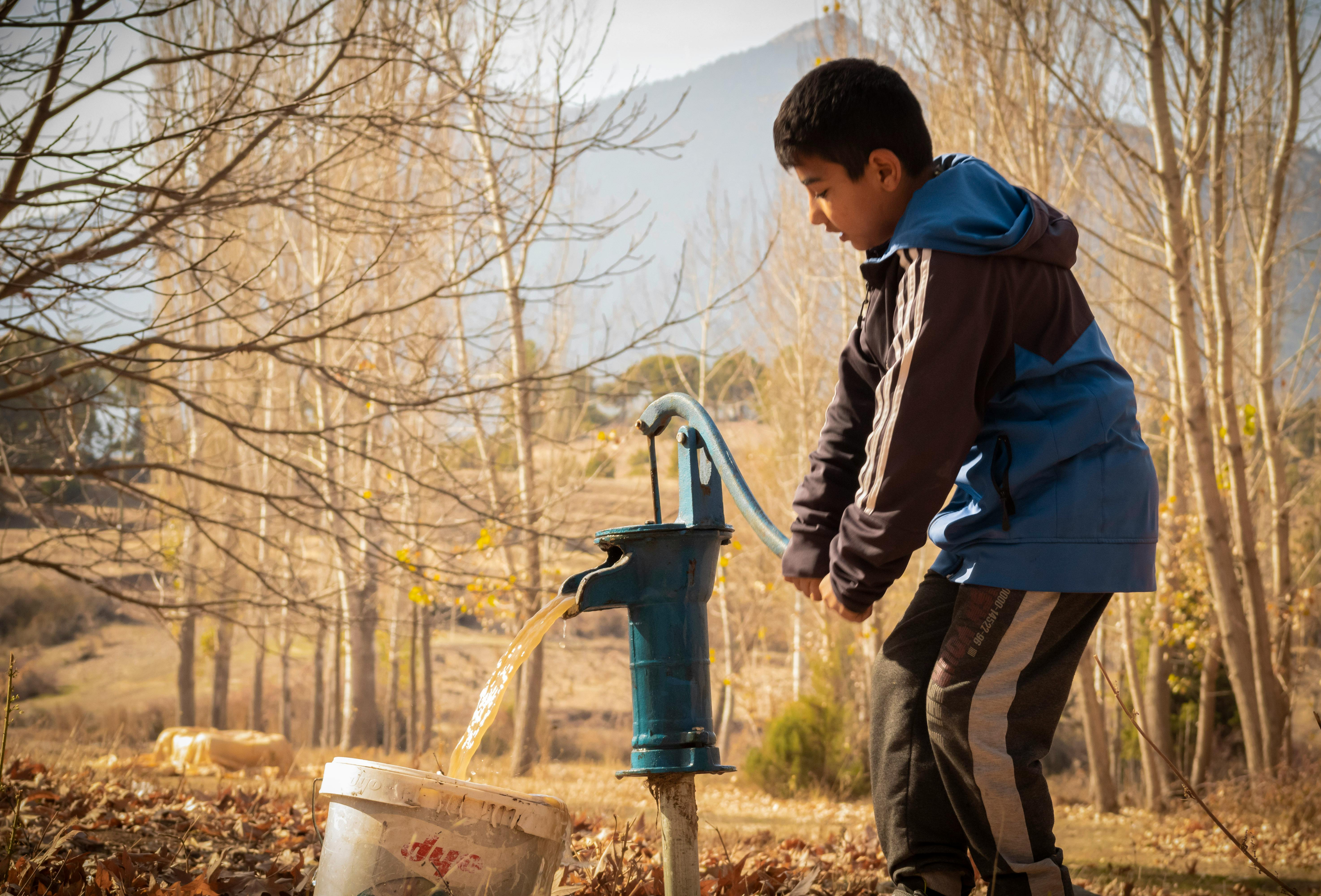 A young boy pumps water in a rural setting during autumn in Pozantı, Turkey.