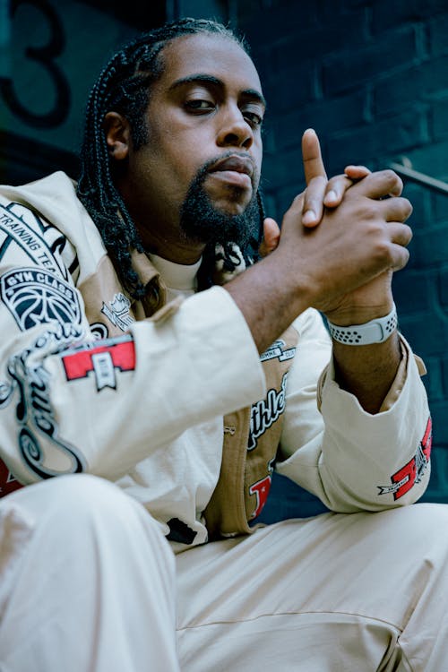 A Man in Printed Jacket Sitting on the Street with His Hands Together