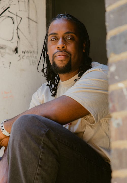 A Man in White Shirt Sitting Near the Concrete Wall