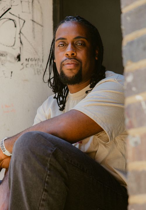 Free Portrait of a serious man sitting by a concrete wall with graffiti. Stock Photo