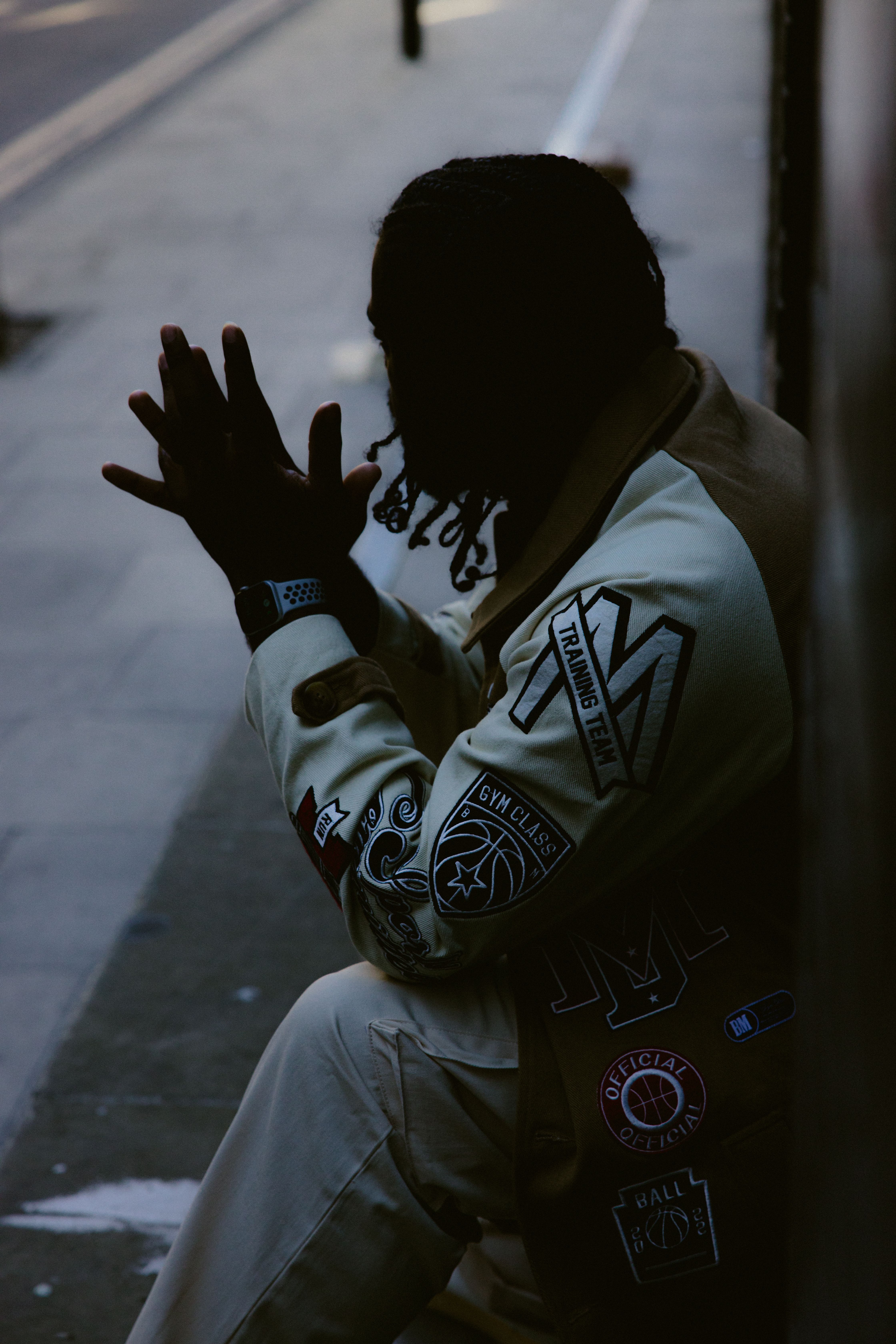 African American man with dreadlocks sitting stylishly on an urban sidewalk, showcasing street fashion.