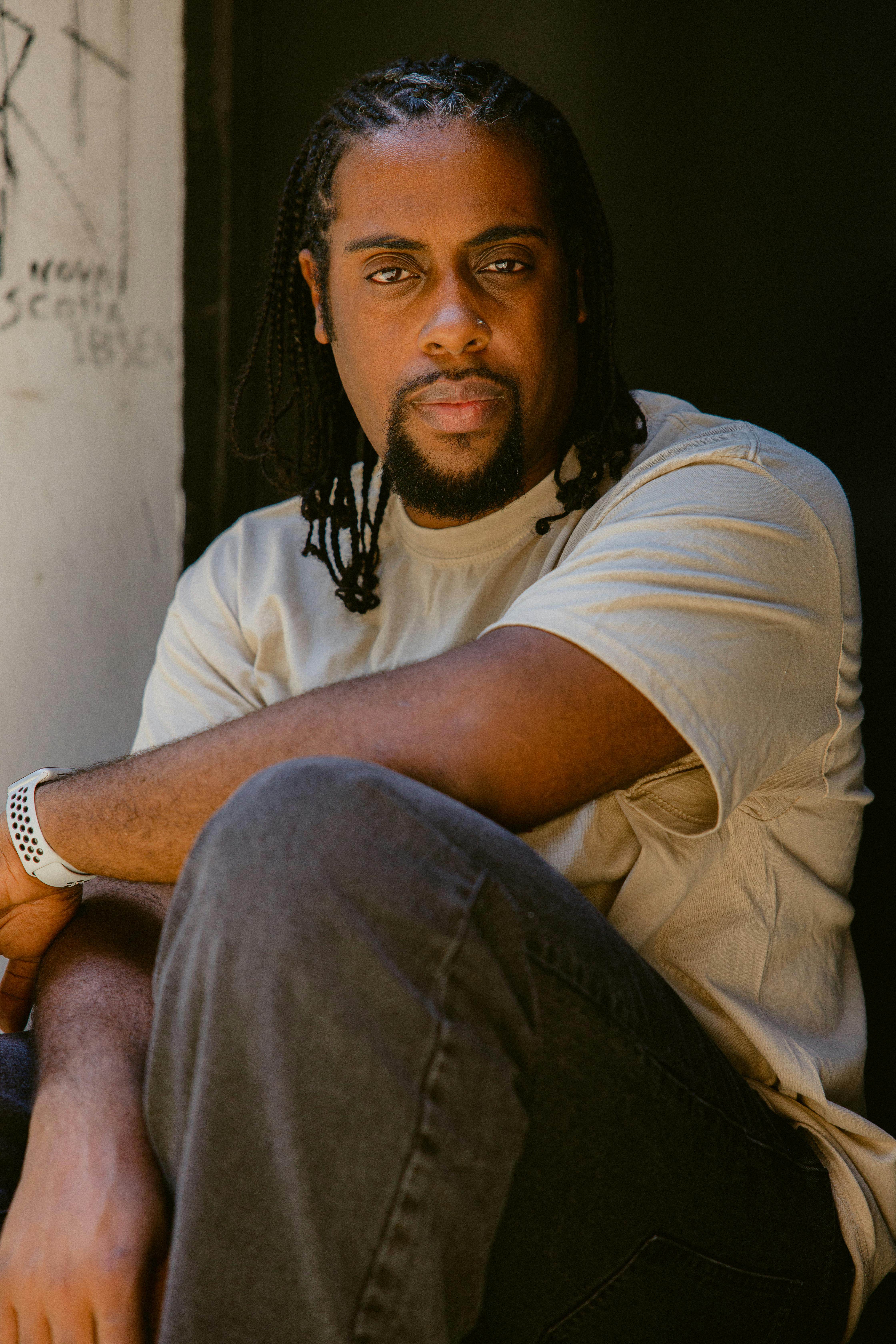 Portrait of a man with braids and goatee sitting indoors in natural light.