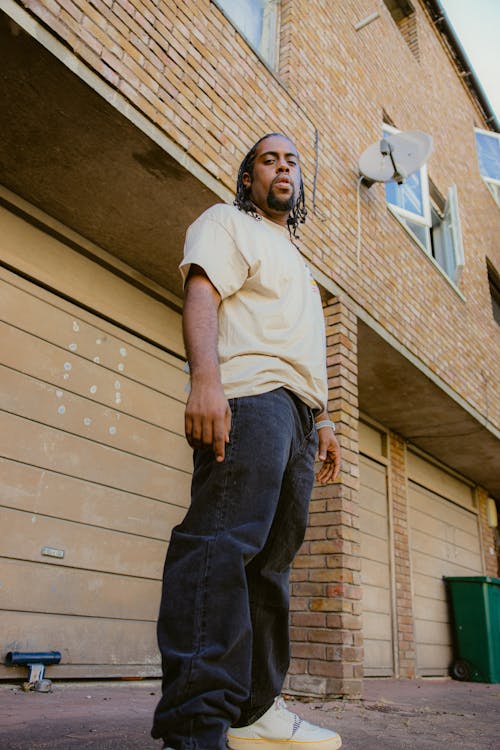 A Low Angle Shot of a Man in White Shirt Standing Near the Brick House