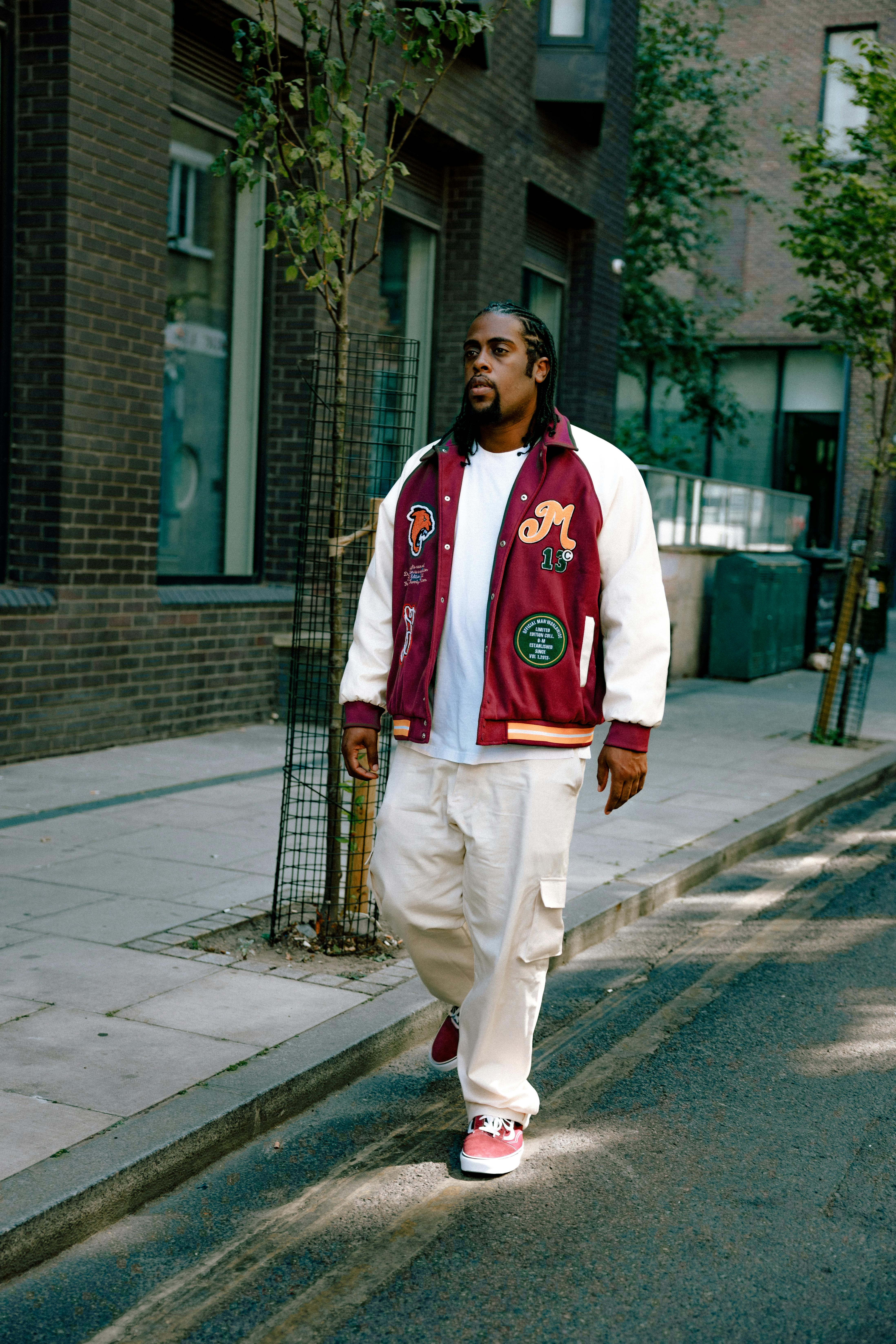 man in white and red zip up jacket and white pants standing on sidewalk