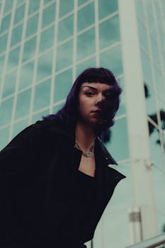 A striking portrait of a woman with purple hair in front of a modern glass building.