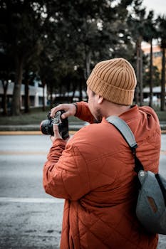 Man taking street photo with a camera in an outdoor urban setting wearing a beanie and jacket.
