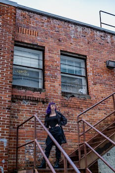 Moody portrait of a woman standing on a staircase against a brick wall with graffiti.