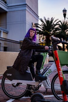A person with vibrant purple hair riding a Lime e-bike in an urban area during twilight.