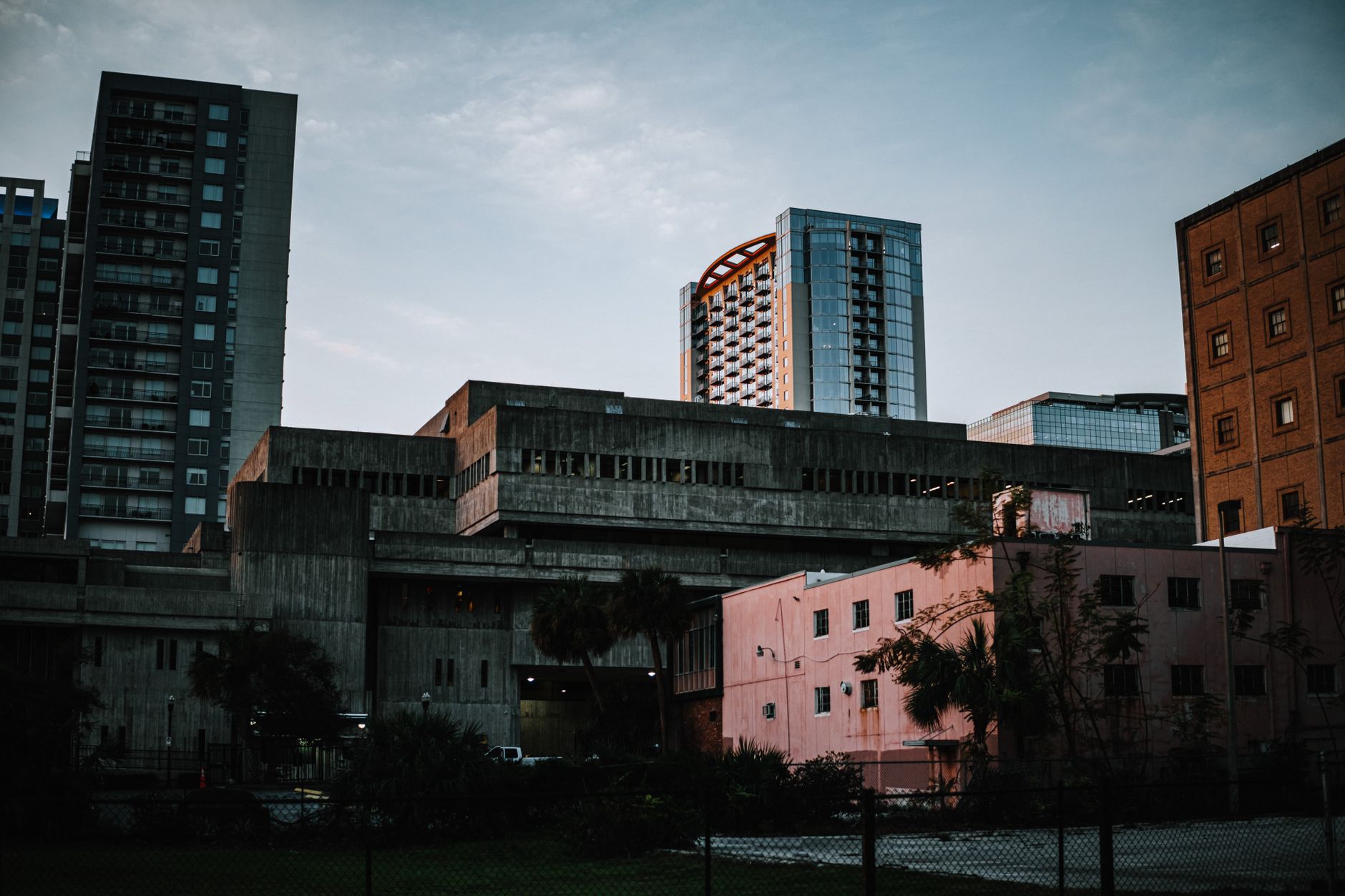 A cityscape featuring diverse buildings and a fence under a dusky sky.