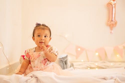 A Young Girl in Floral Dress Sitting on the Bed